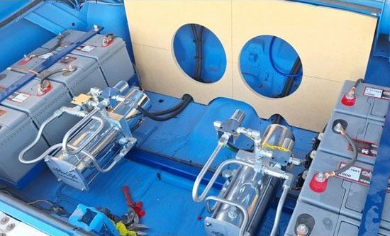 Lowrider car hydraulic system in a blue trunk with batteries and pumps. A wooden panel has two circular cutouts.