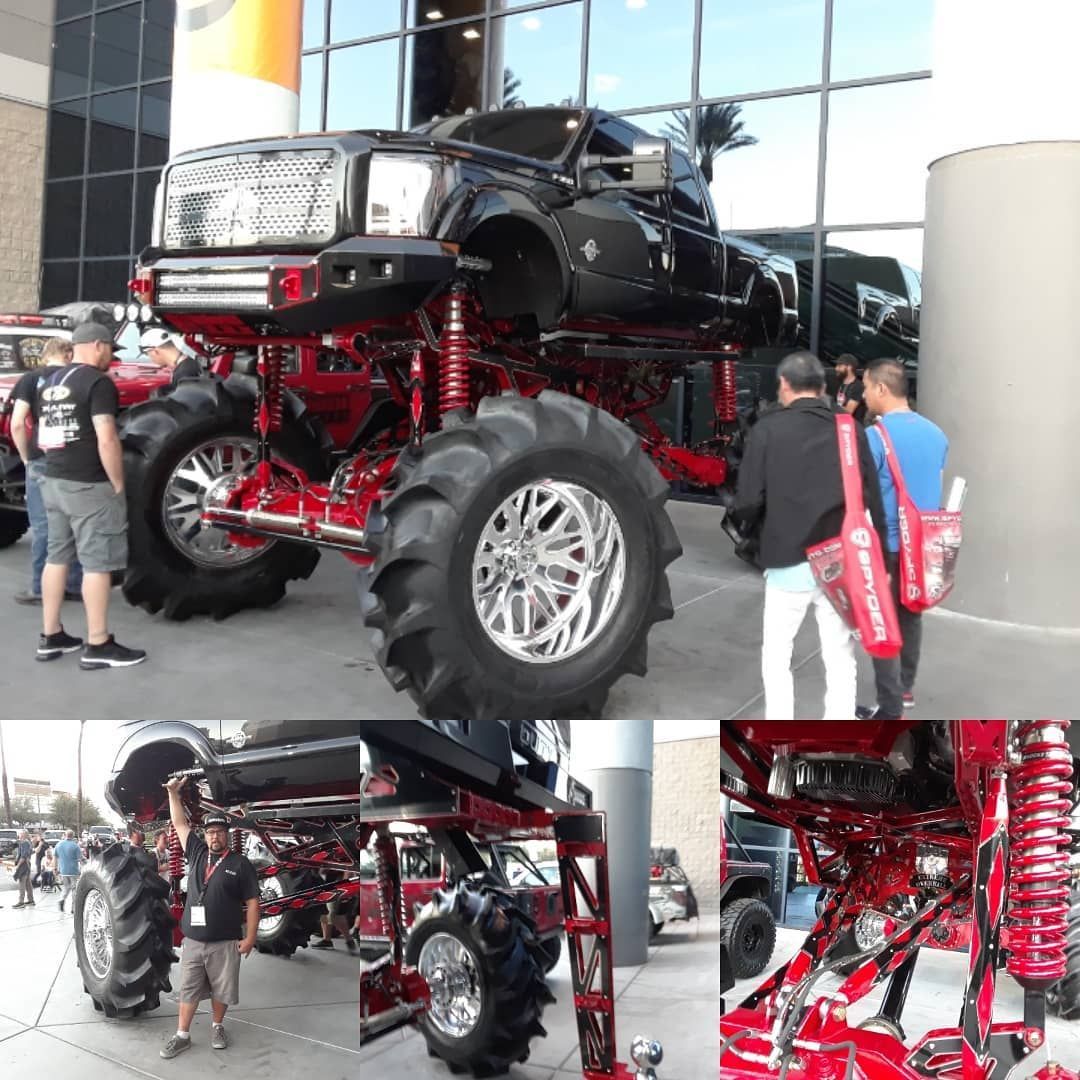 A massive black and red custom lifted truck with large tires displayed at an outdoor event, surrounded by people.