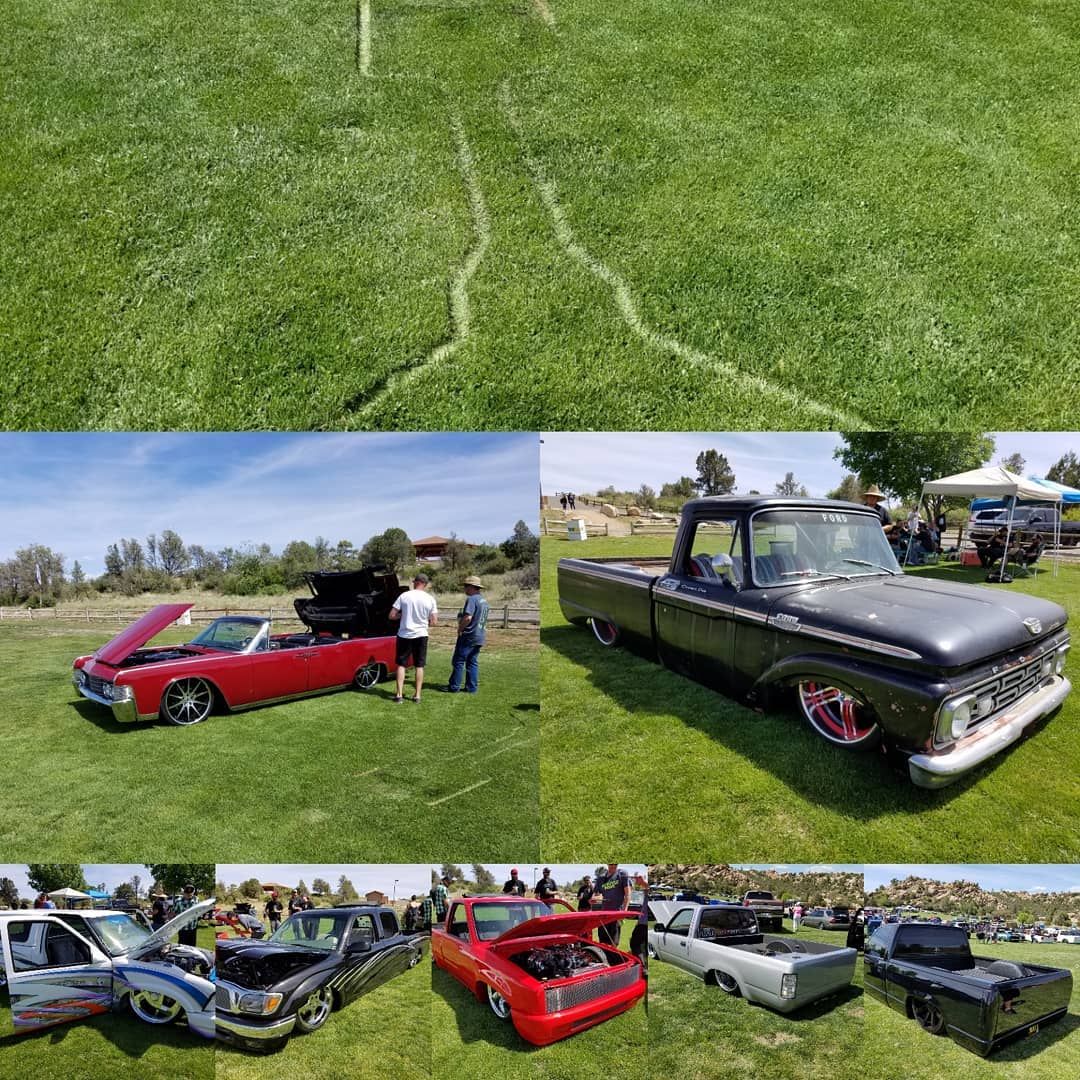 A car show on a grassy field. Several classic trucks are parked on the lawn, with attendees viewing the vehicles.