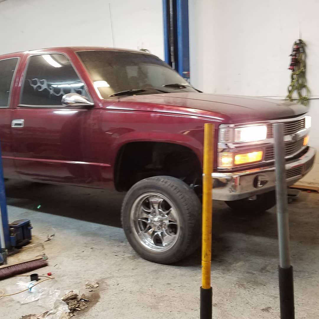 A maroon pickup truck in a garage with chrome wheels and bright headlights.