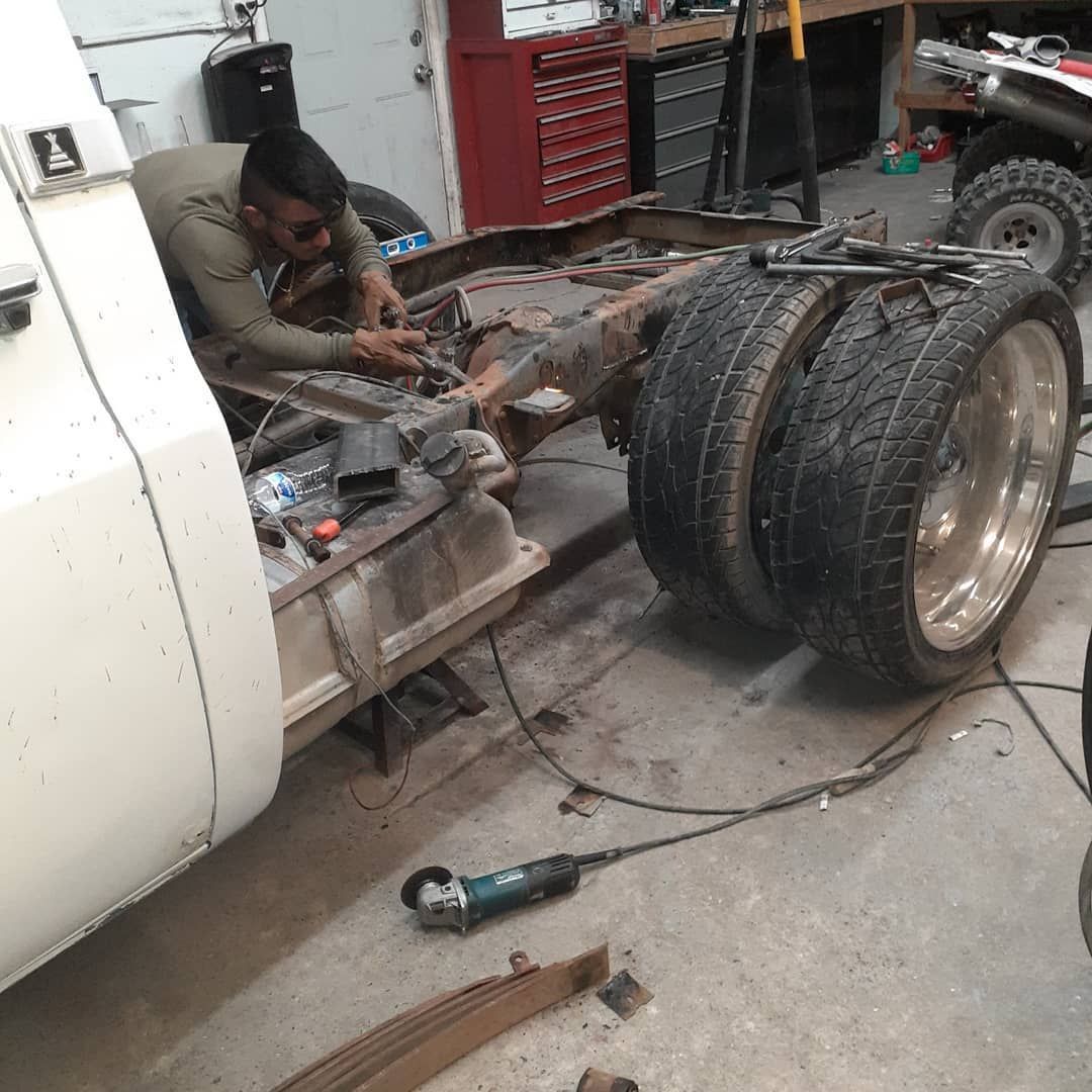 Man working on a truck chassis in a garage. He's wearing a green shirt. The truck has large dual rear wheels.