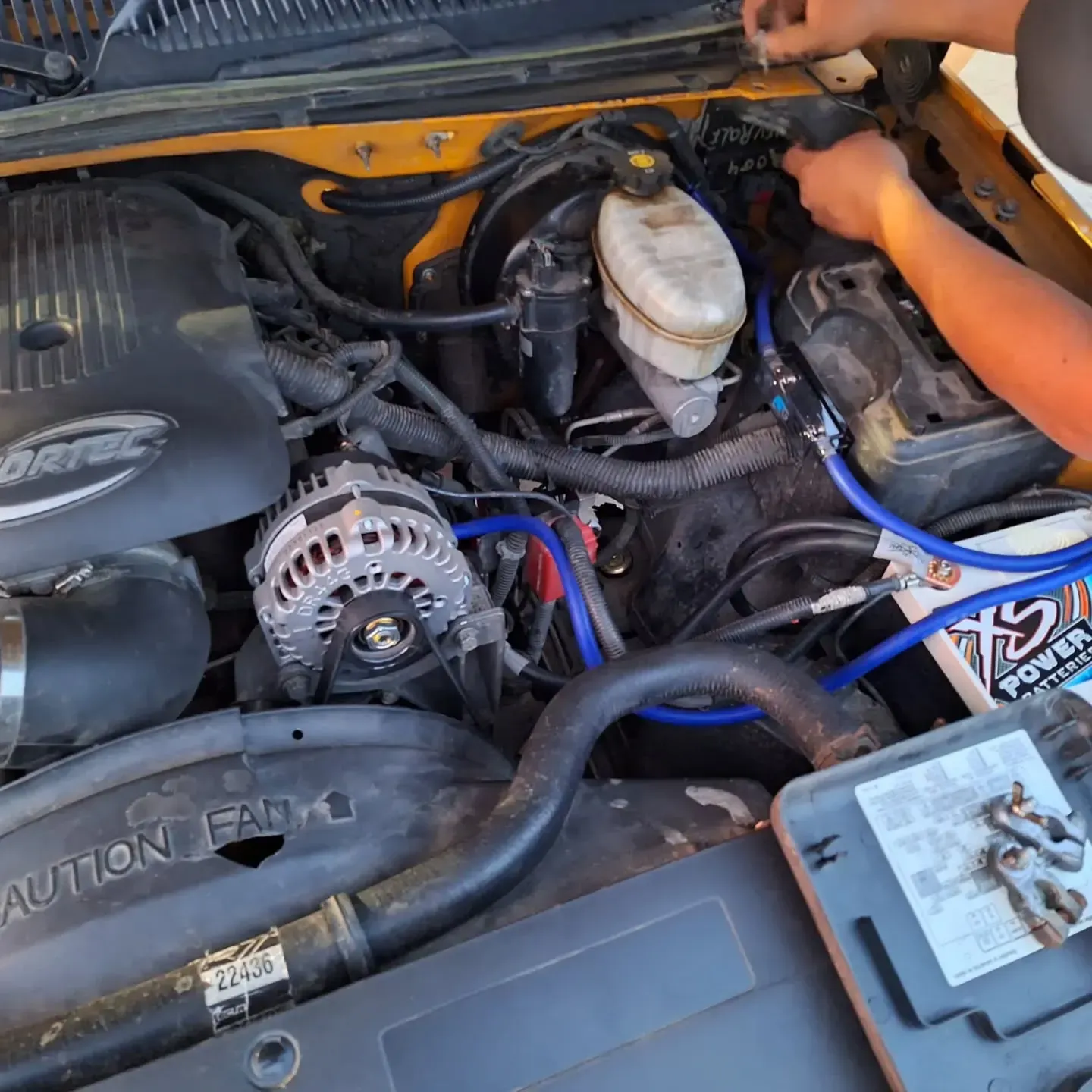 Person working on a yellow truck's engine bay, visible com