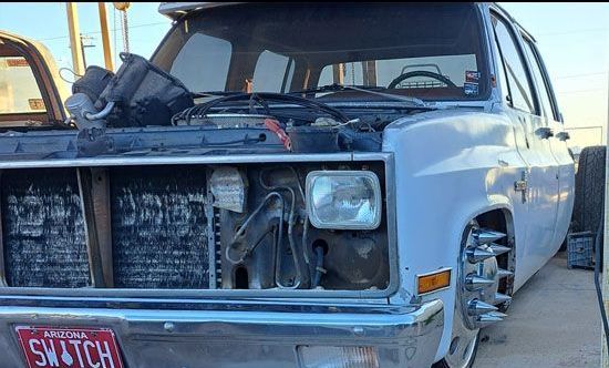 A white Chevrolet Suburban with the hood open, showing the engine components. It's in a parking area.