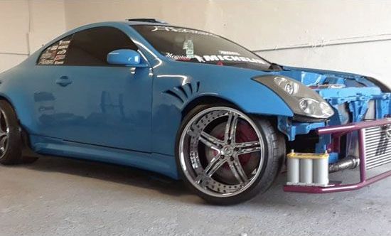 Blue modified car with custom chrome wheels, missing the front bumper and hood.