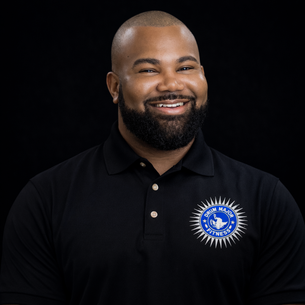 A smiling person with a beard, wearing a black polo shirt with a circular logo on the chest, set against a black backdrop.