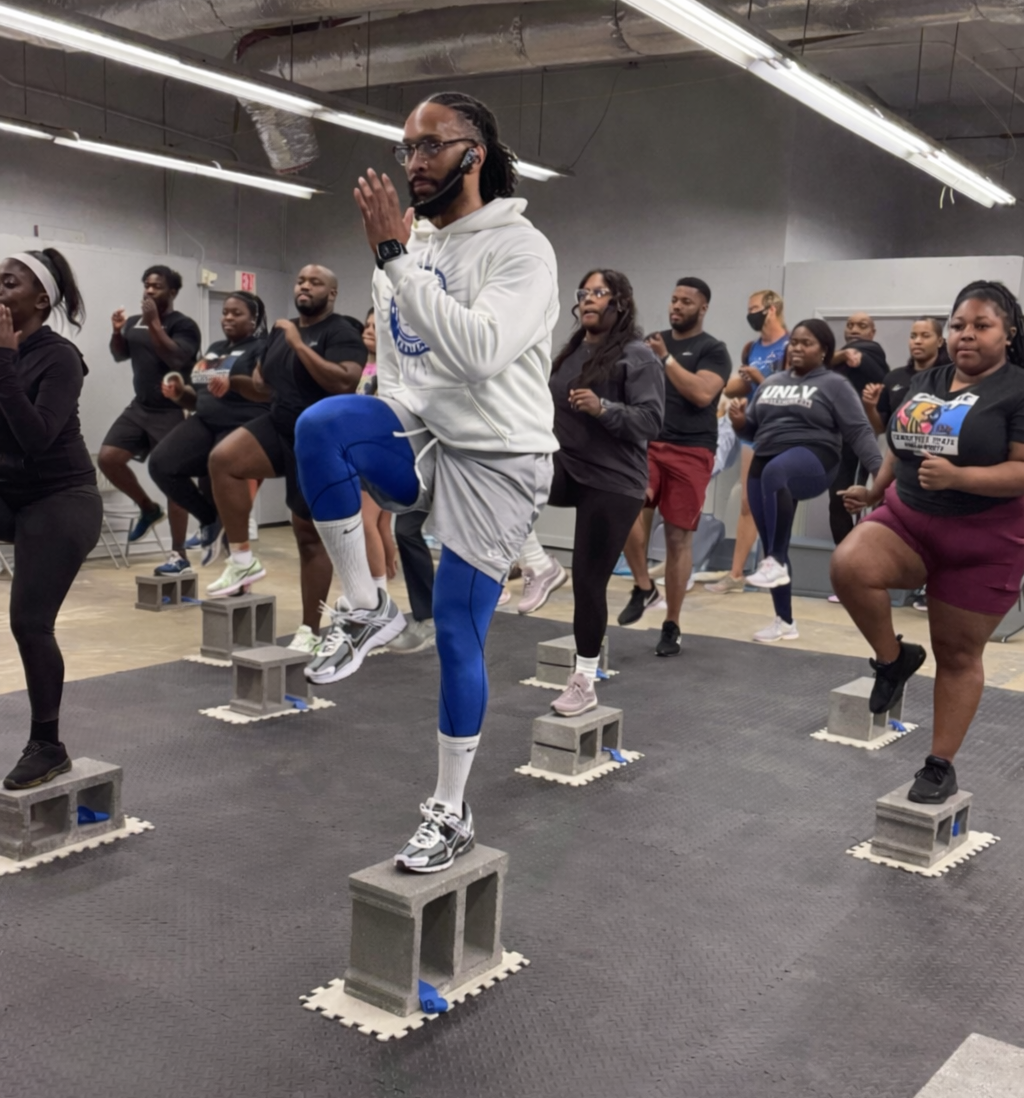 A group of people perform high-knee exercises on individual concrete blocks in a fitness class.