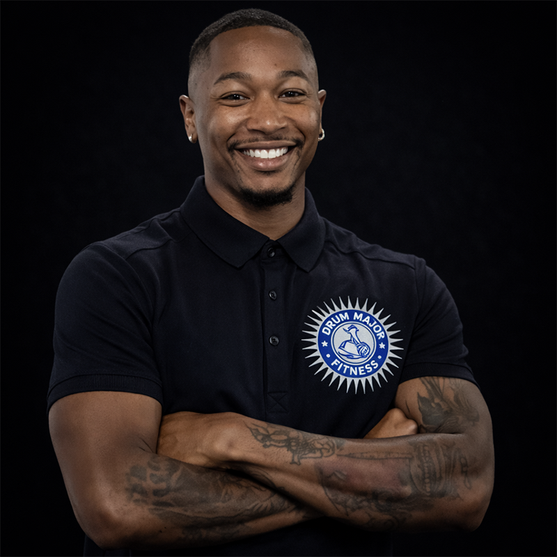 A smiling person wearing a black polo shirt with a Drum Major Fitness logo, standing with arms crossed against black.