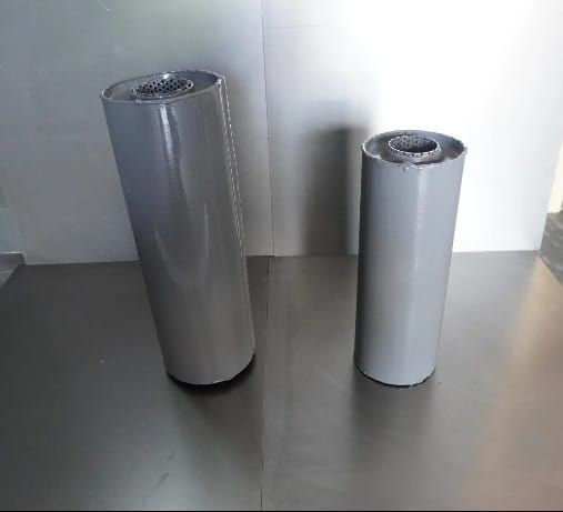 Dos objetos cilíndricos grises sobre una superficie metálica, ligeramente inclinados hacia la izquierda.