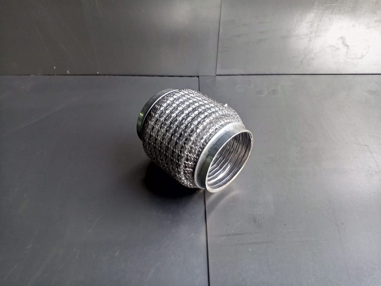 Tubo de escape de metal flexible sobre una superficie oscura.