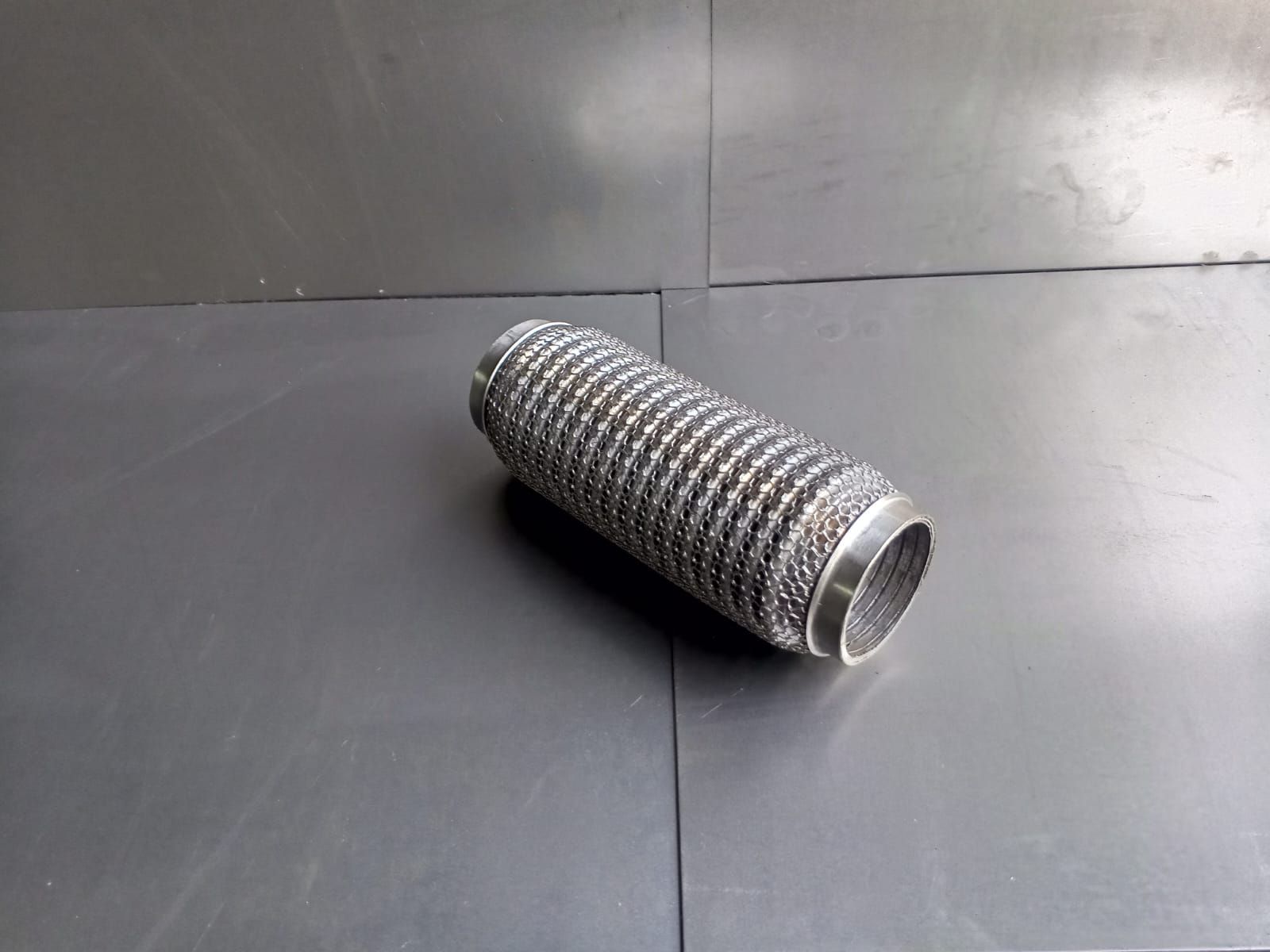 Tubo de escape de metal flexible sobre una superficie oscura.