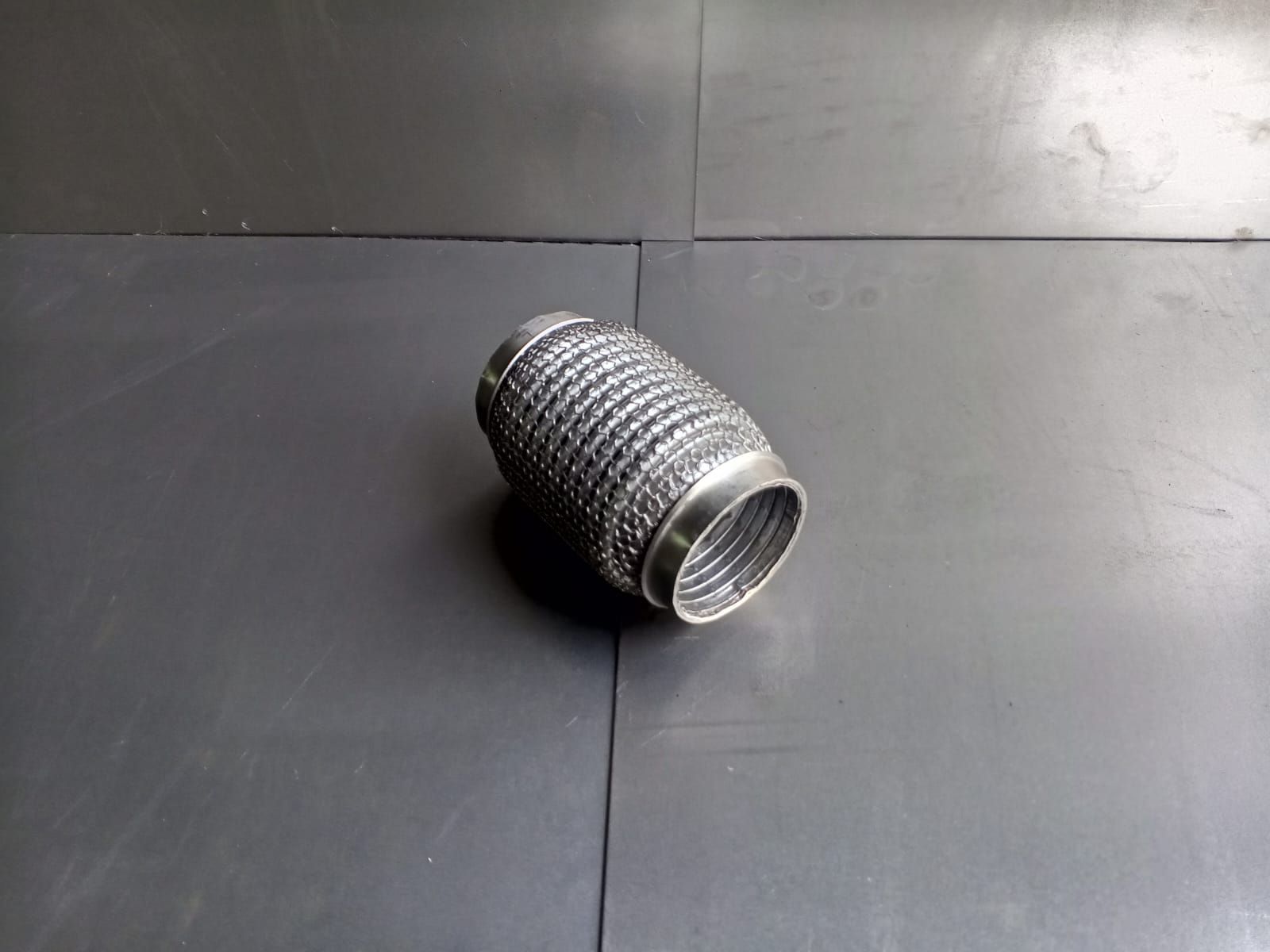 Tubo flexible de escape de metal sobre una superficie oscura.