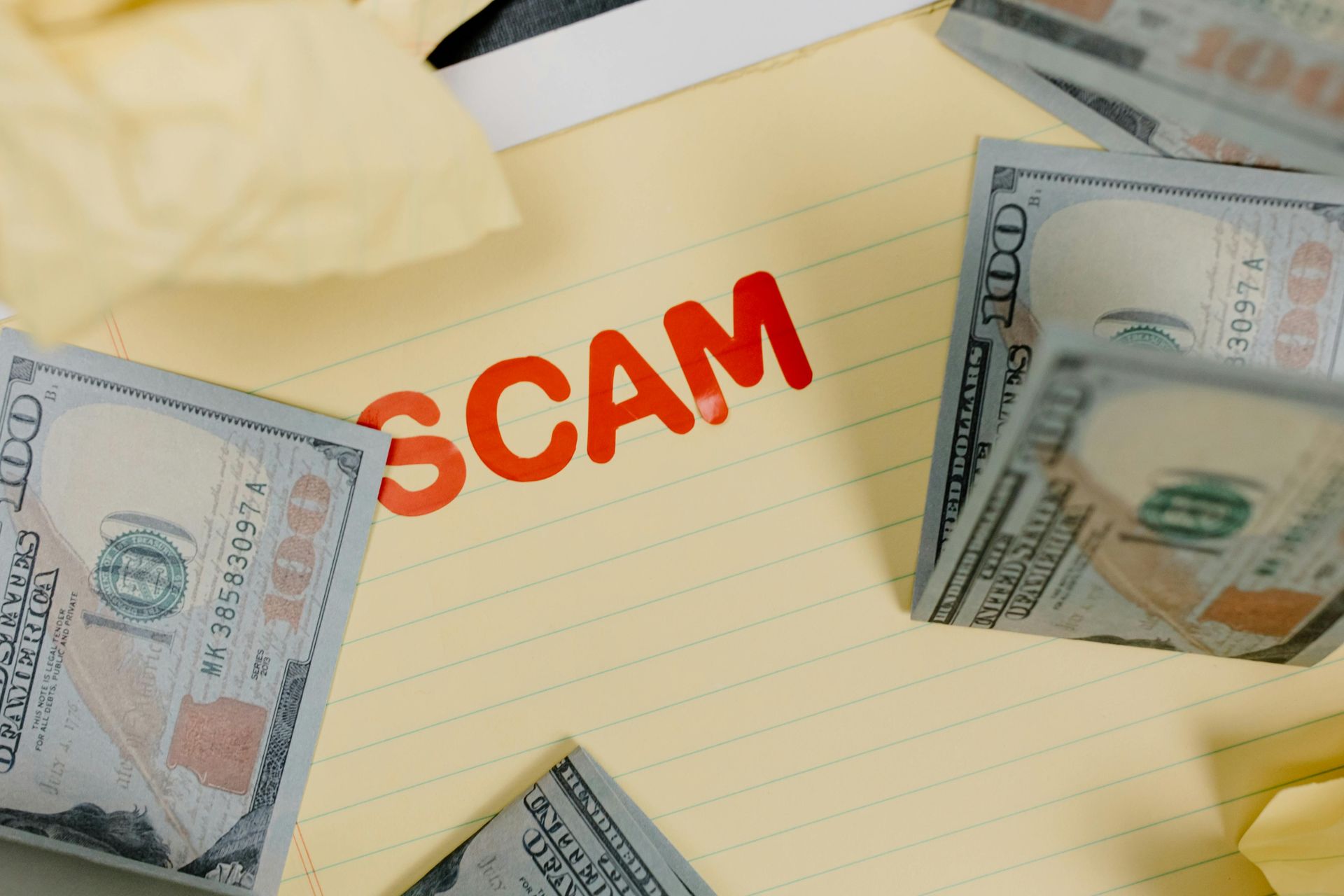 The word scam is written on a piece of paper next to a pile of money.