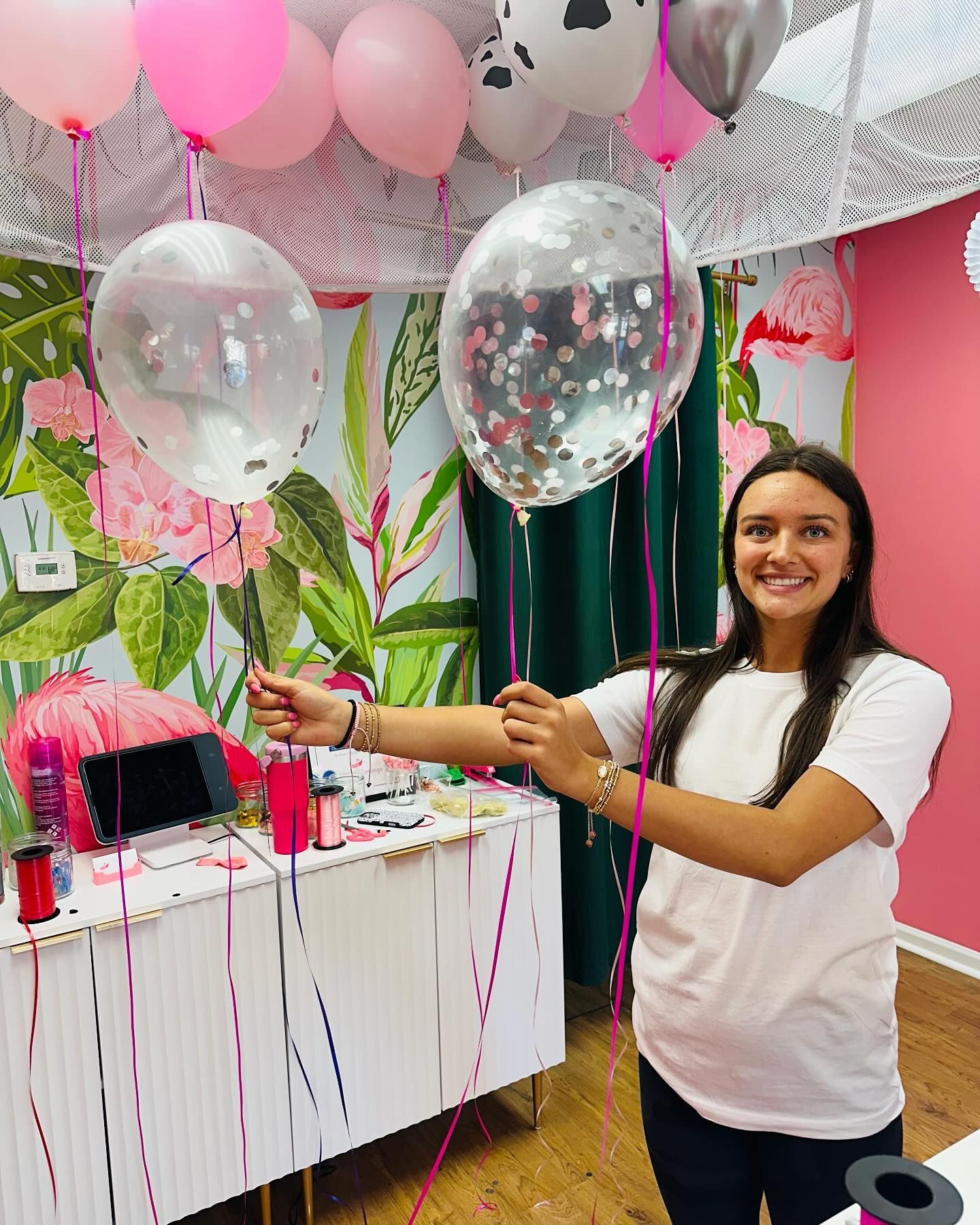 A woman is standing in a room with balloons hanging from the ceiling.