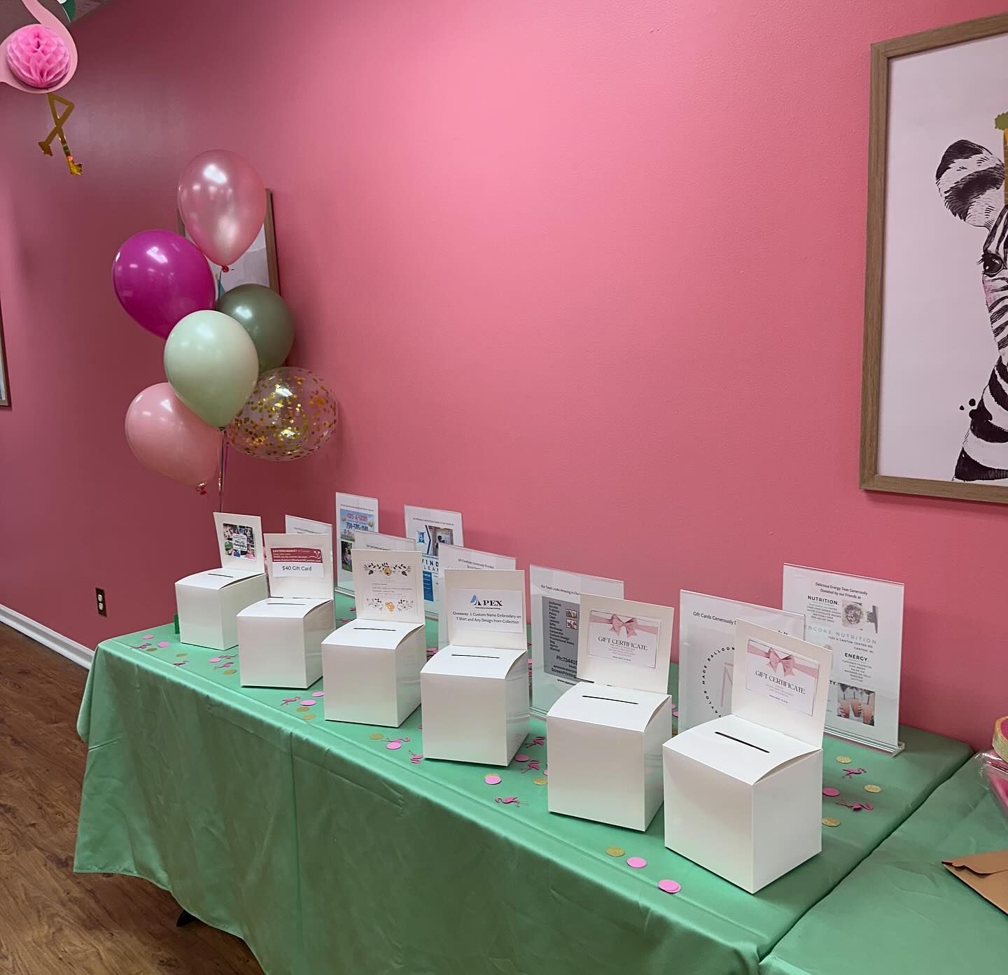 A table with boxes and balloons on it in front of a pink wall.