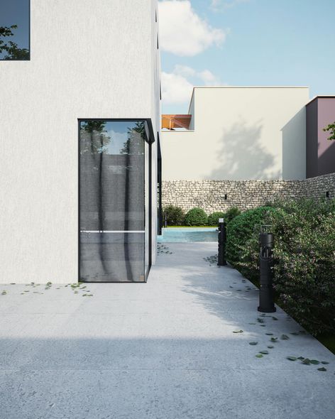 Modern white buildings with a walkway alongside a stone wall and lush greenery.