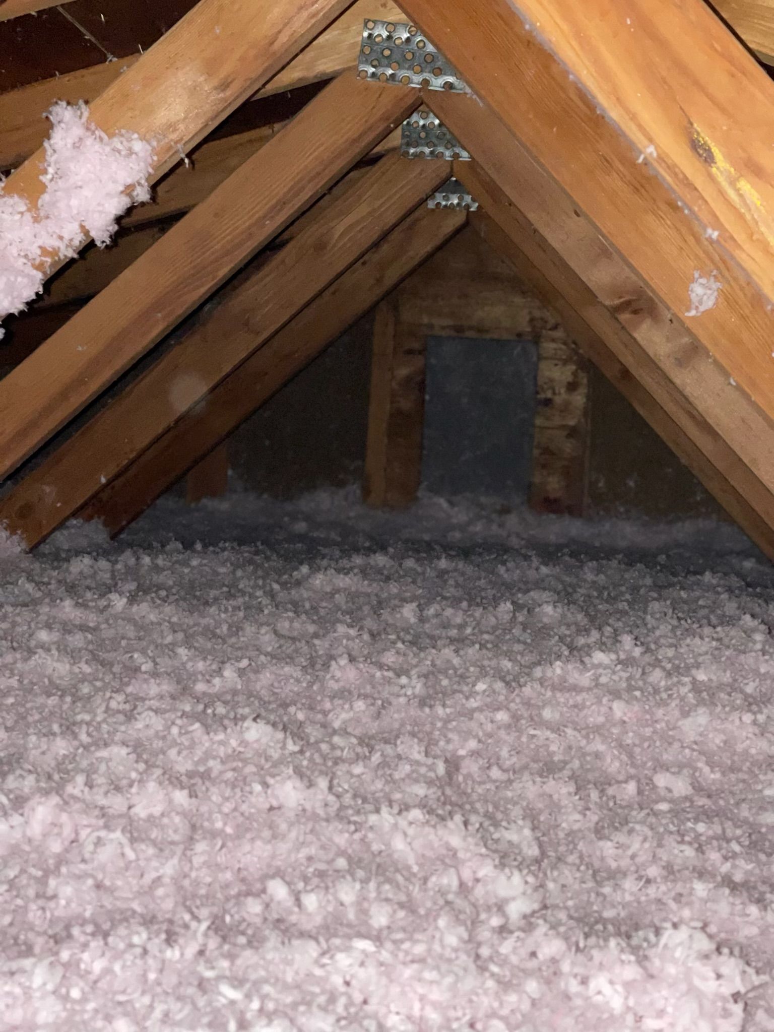 An attic with a lot of white insulation and wooden beams