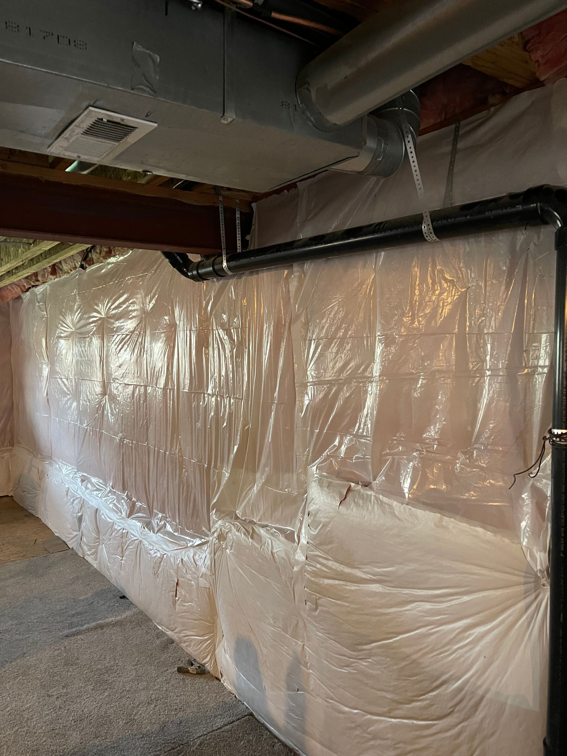 A basement with a wall covered in plastic and pipes.