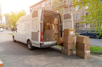 A white delivery van is parked on the side of the road with boxes in the back.