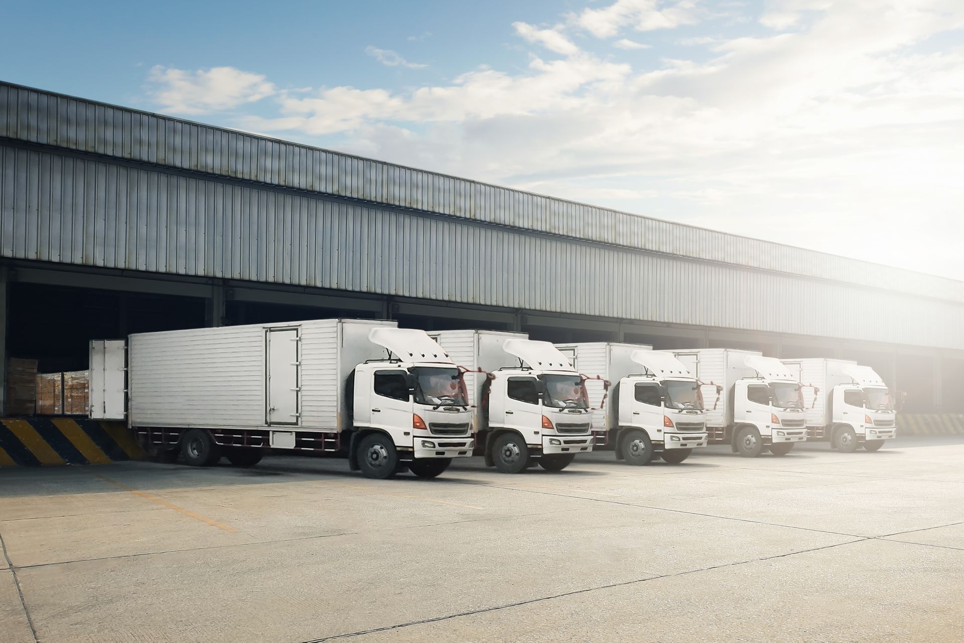 A row of white trucks are parked in front of a warehouse.