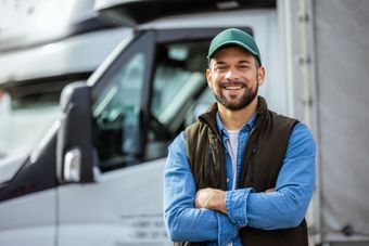 A man is standing in front of a truck with his arms crossed.