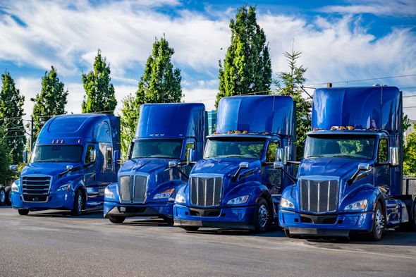 A row of blue semi trucks are parked in a parking lot.