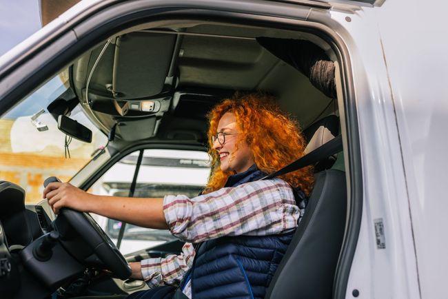 A woman is sitting in the driver 's seat of a white van.