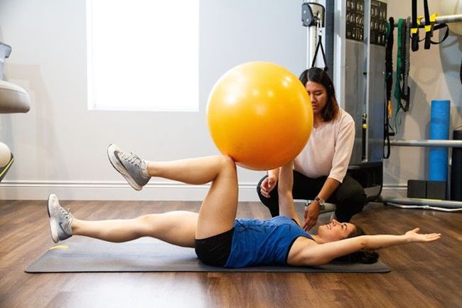 A woman is doing exercises with an orange exercise ball.