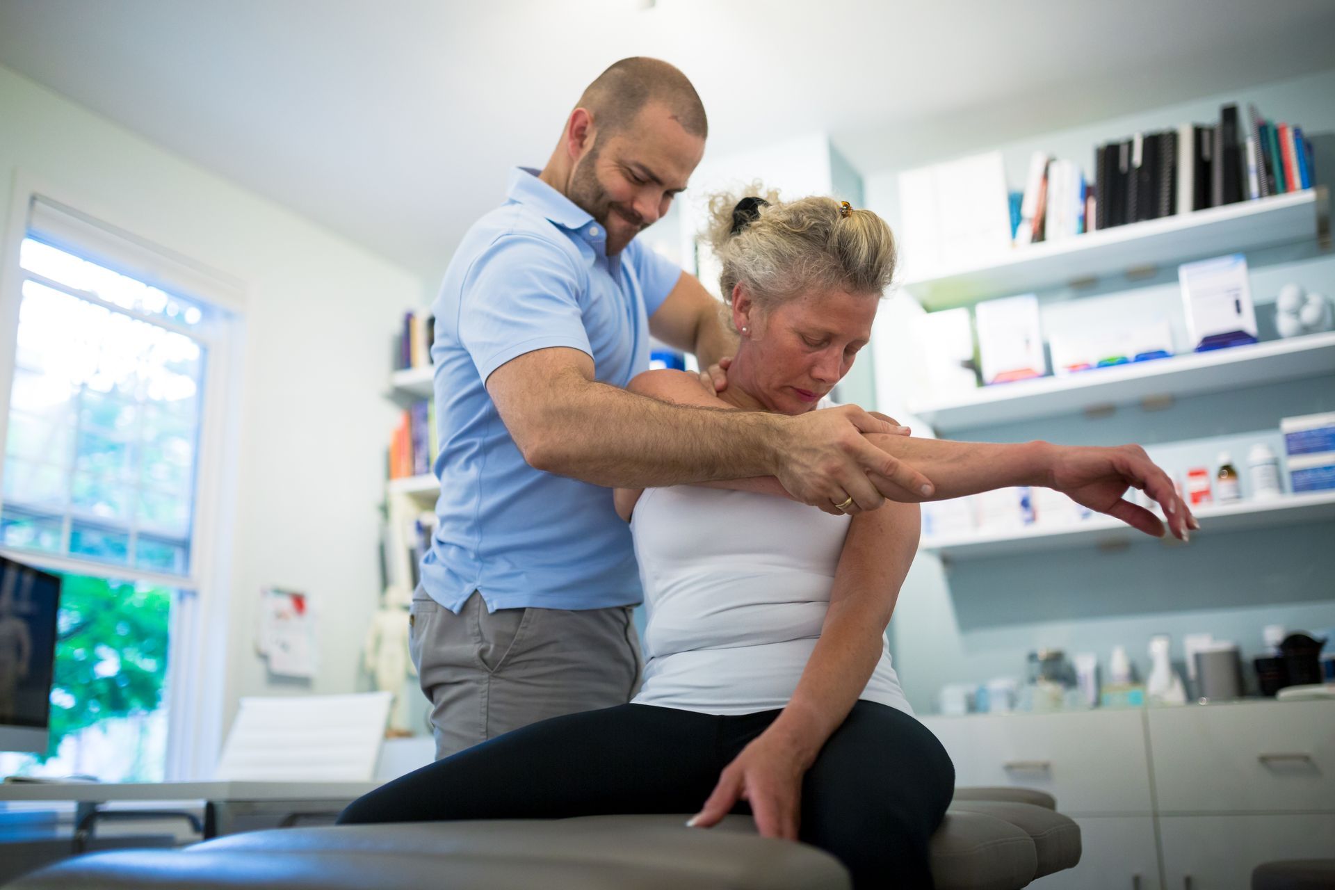A healthcare professional stretches a woman's arm in a medical office, focusing on shoulder mobility.