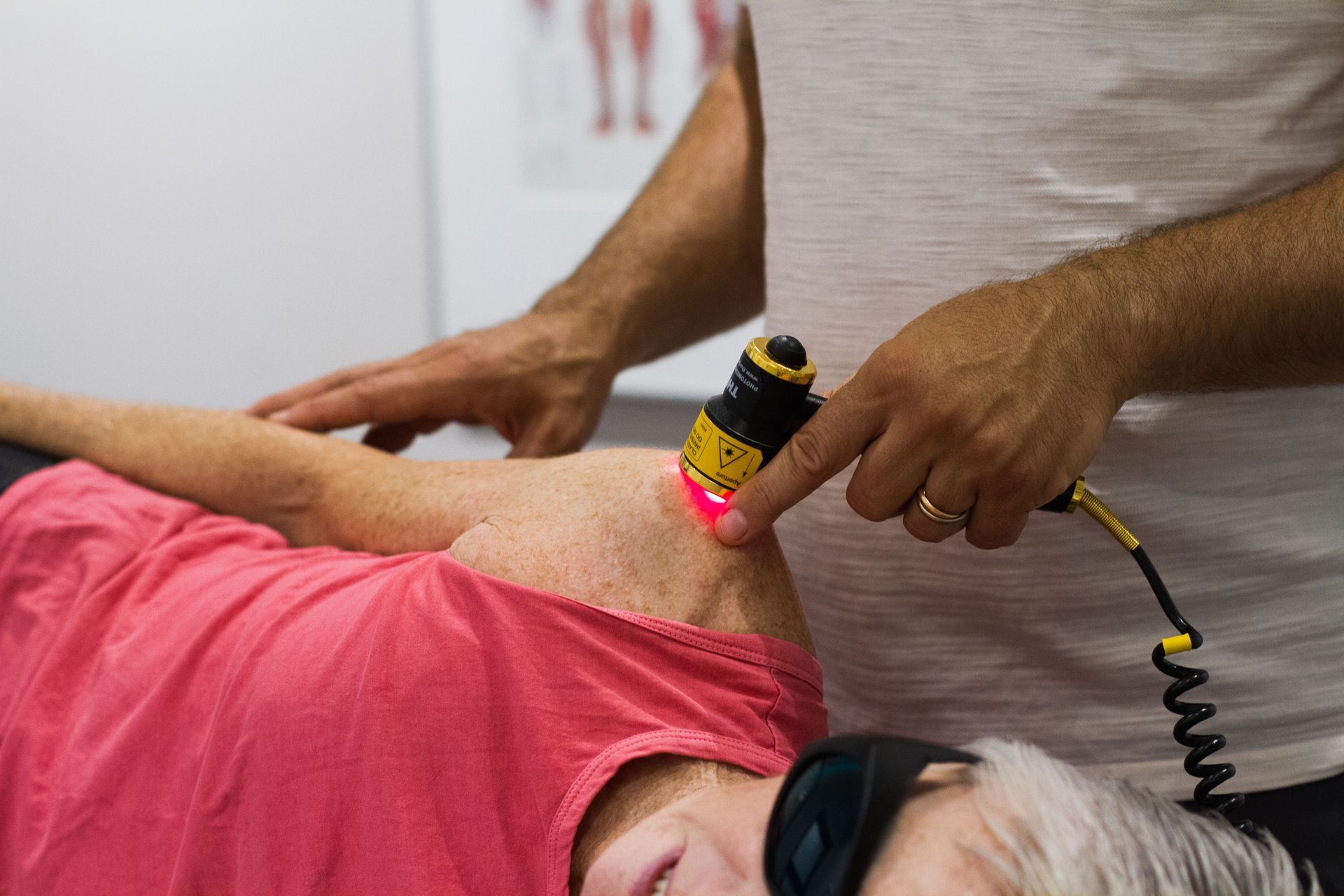 Person receiving laser therapy on shoulder. Therapist holds device, targeting treatment area.