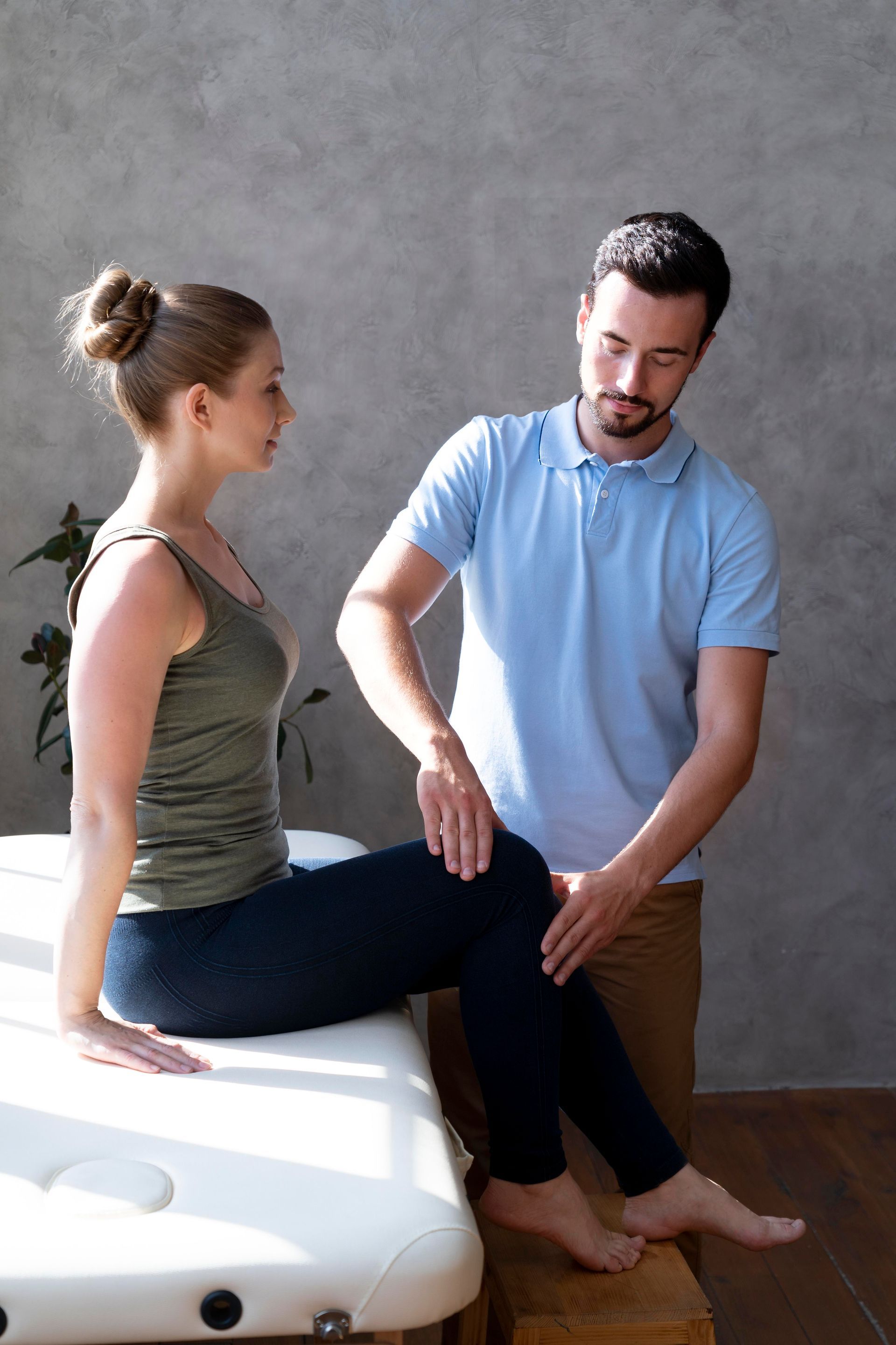 A man is helping a woman stretch her leg on a table.