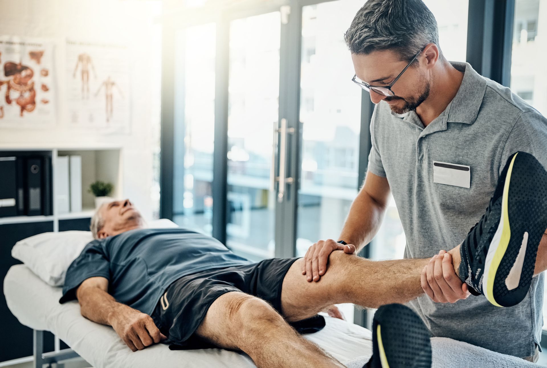 A man is laying on a bed while a physical therapist stretches his leg.