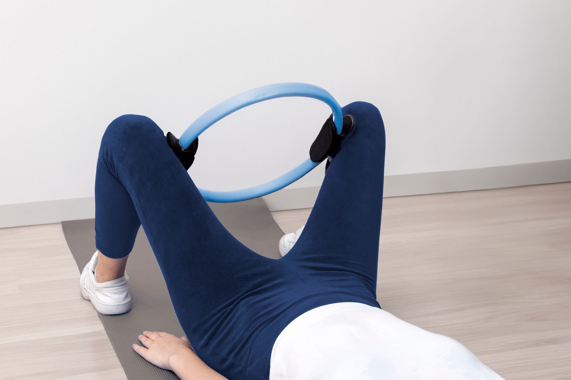 A woman is laying on a yoga mat using a pilates ring.