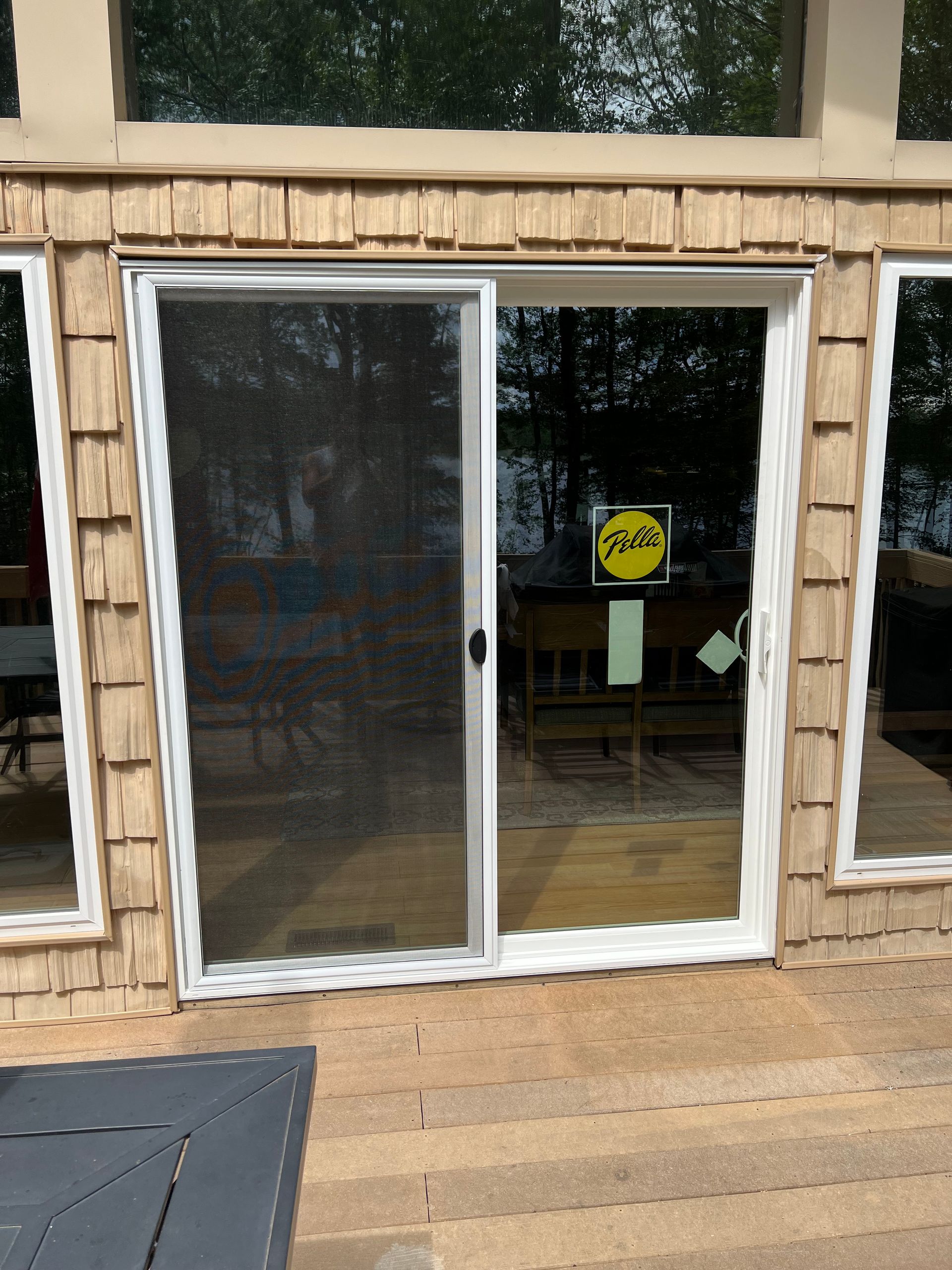 Sliding glass door with a screen door on a wooden deck, surrounded by windows and cedar siding.