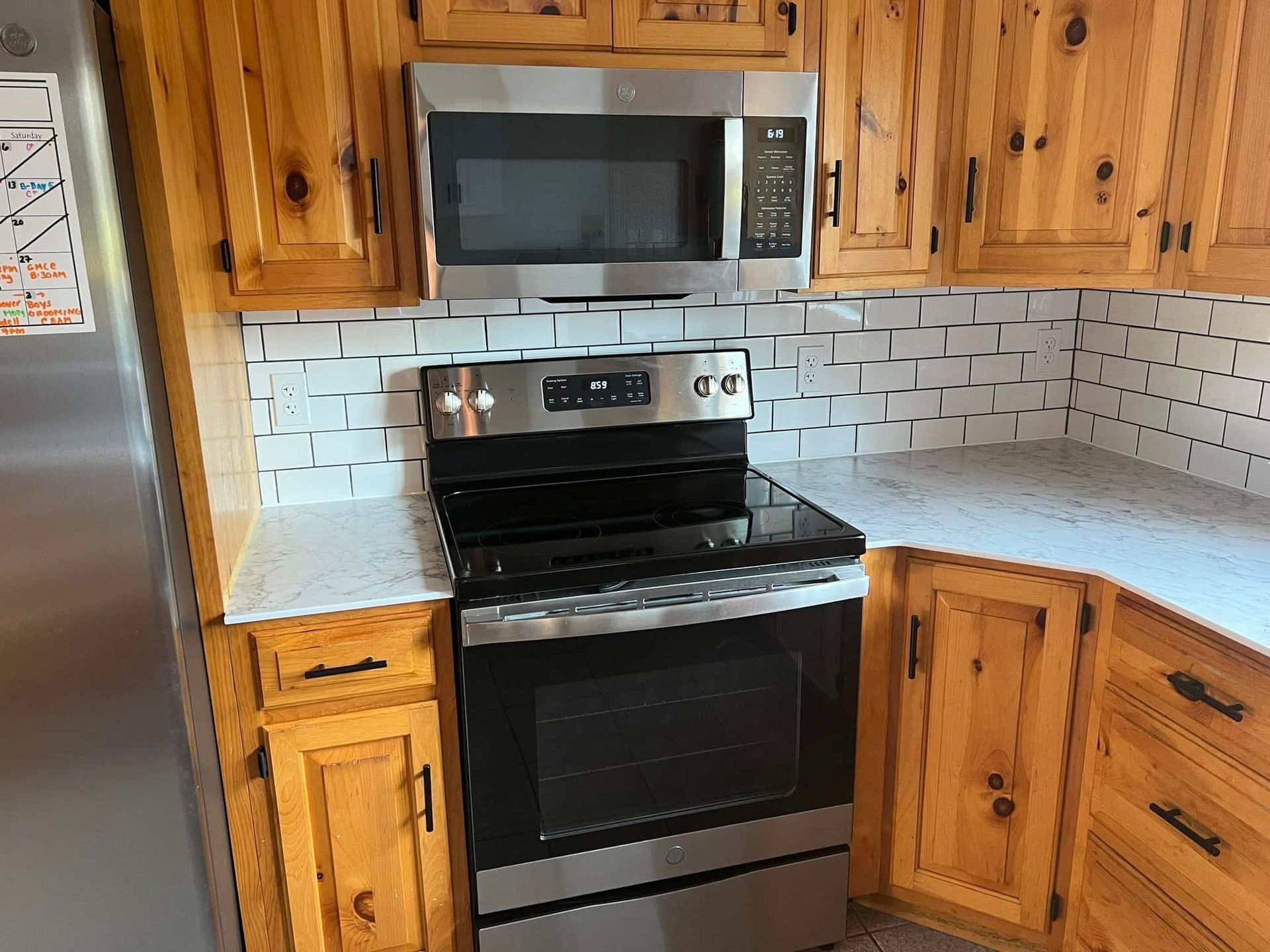 Kitchen with stainless steel appliances: microwave, range, and refrigerator. Light wood cabinets, white backsplash.