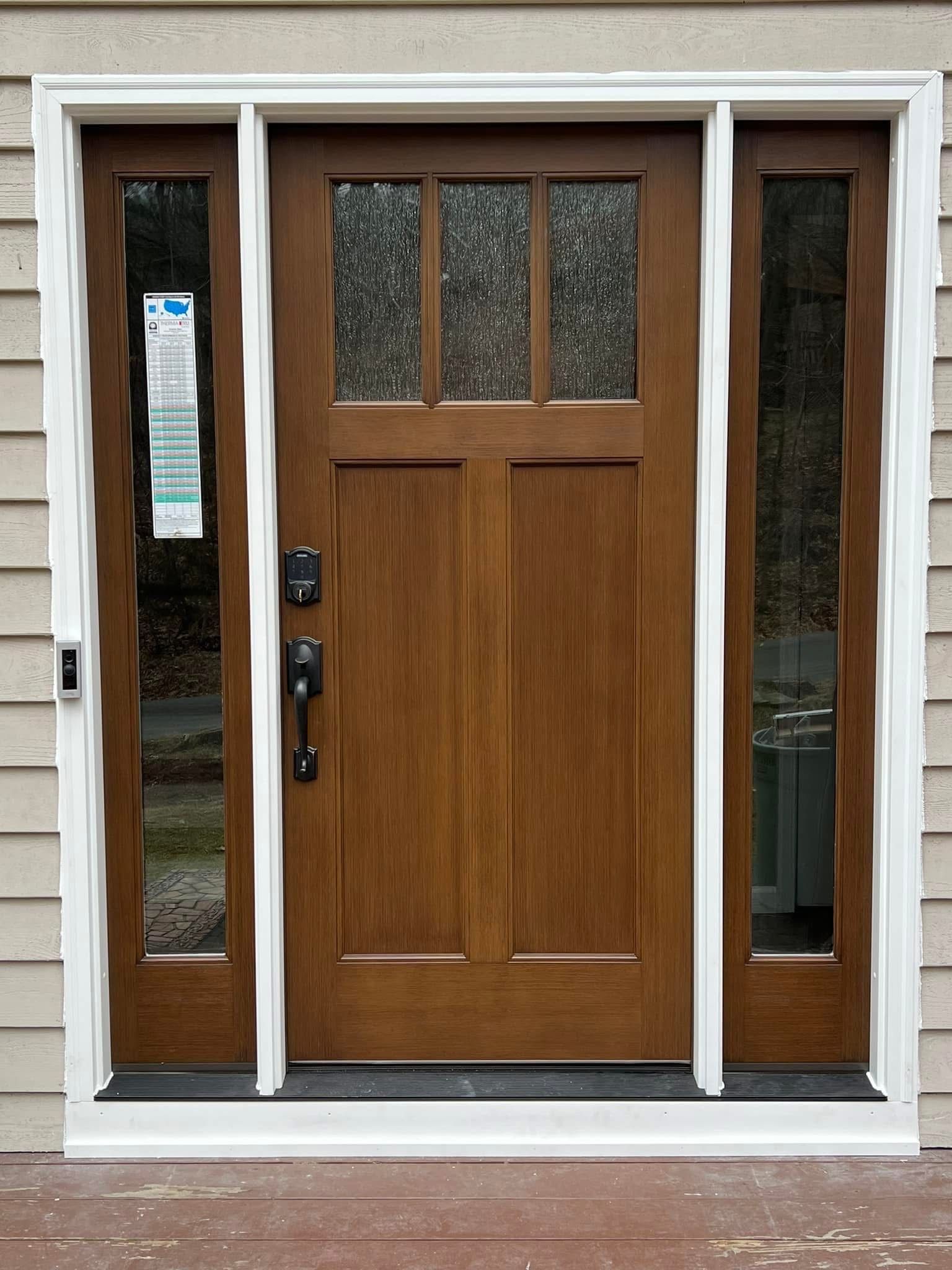 Brown Craftsman-style door with sidelights, framed in white trim. The door has glass panes in the top section, and the sidelights are clear.