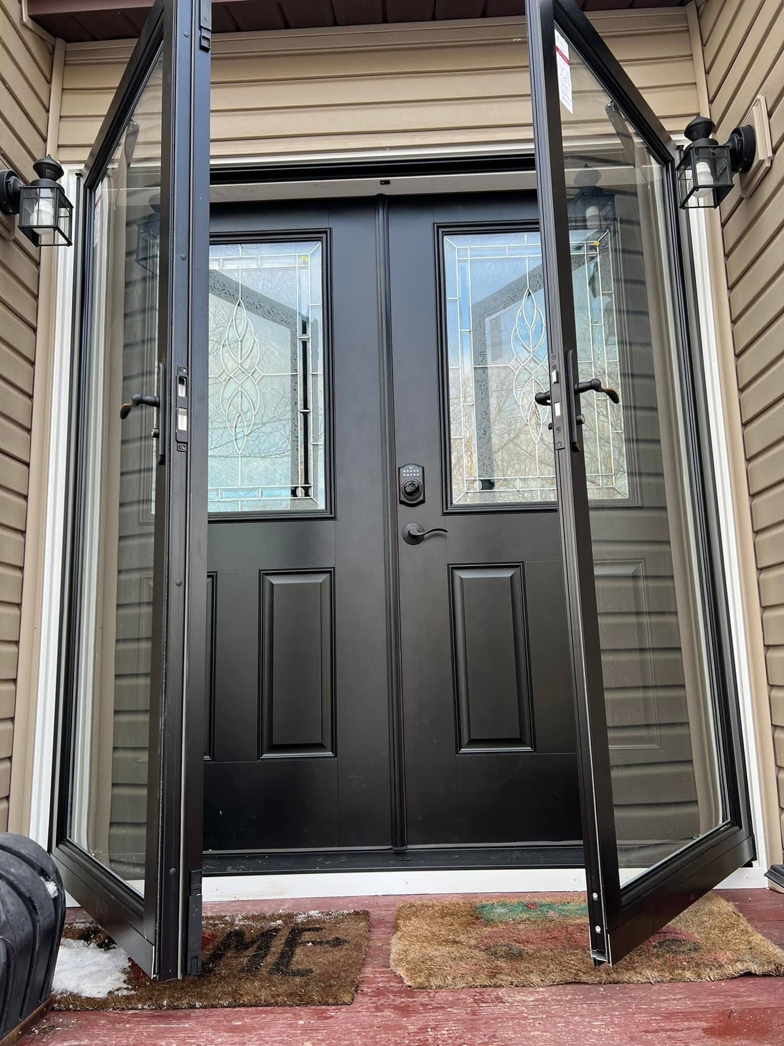 Black double doors with sidelights opening outwards. The front door is black, with glass panes in the sidelights and top panels.
