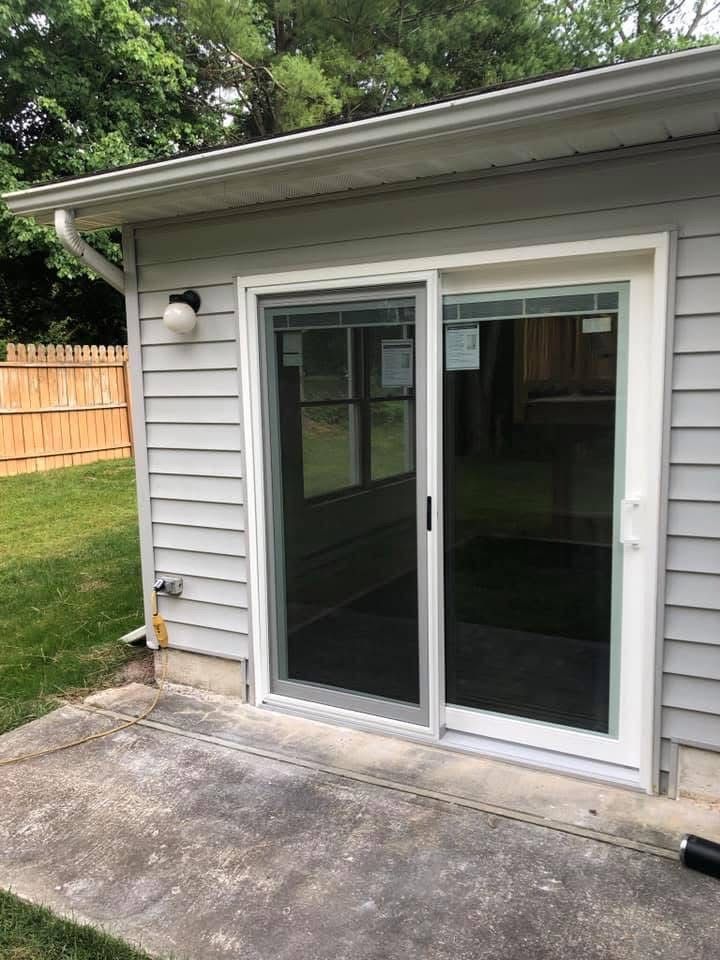 Sliding glass door set into a gray siding wall on a concrete patio, with a white trim.