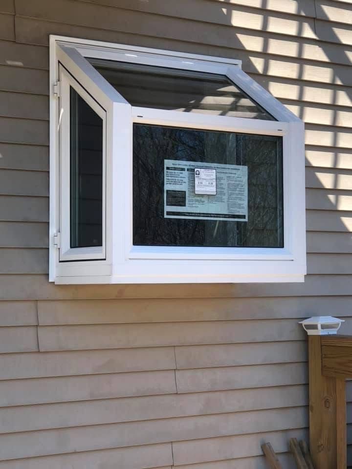 White, angled window on a beige-sided building, partially open. A sheet of newspaper is visible inside the window.