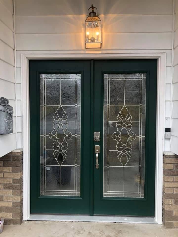 Green double doors with glass panels and decorative design, beneath a lit lantern.