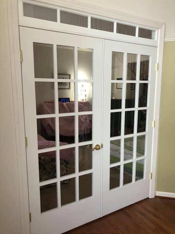 White French doors with multiple glass panes, leading into a room with furniture and a rug; light reflected on the glass.