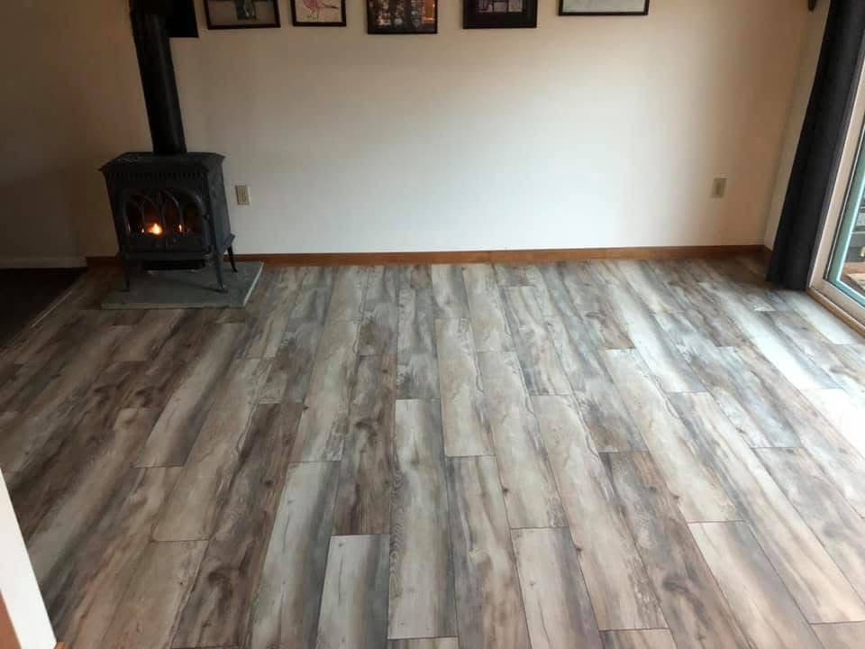 A room with new wood-look flooring, a lit stove, and a white wall with framed photos. Sliding glass door on the right.