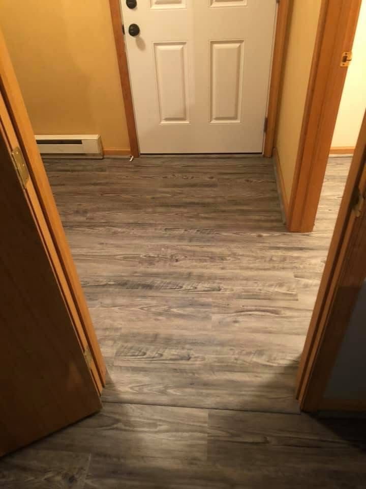 Interior view with new grey wood-look flooring leading to a white door. Two brown doorways frame the view.