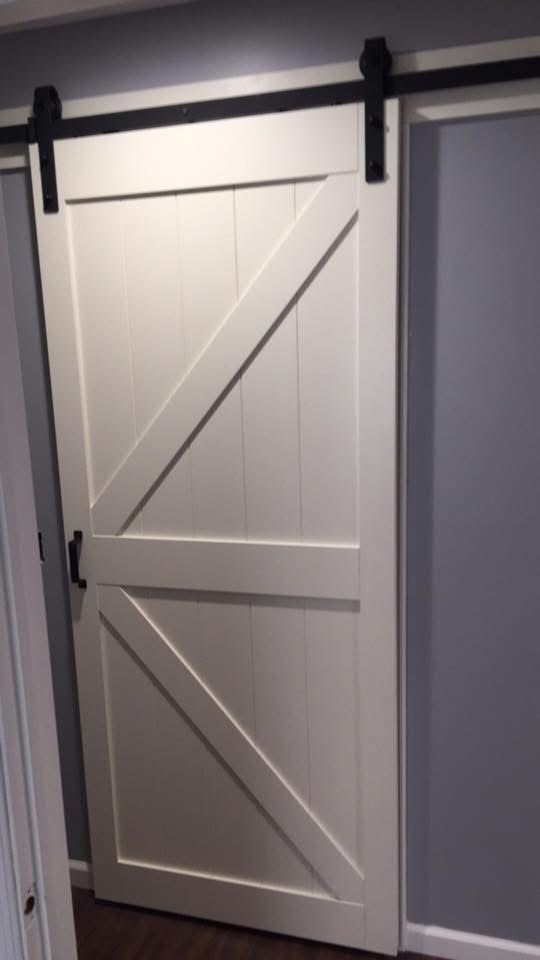 White barn door with black hardware, mounted on a black track against a gray wall.