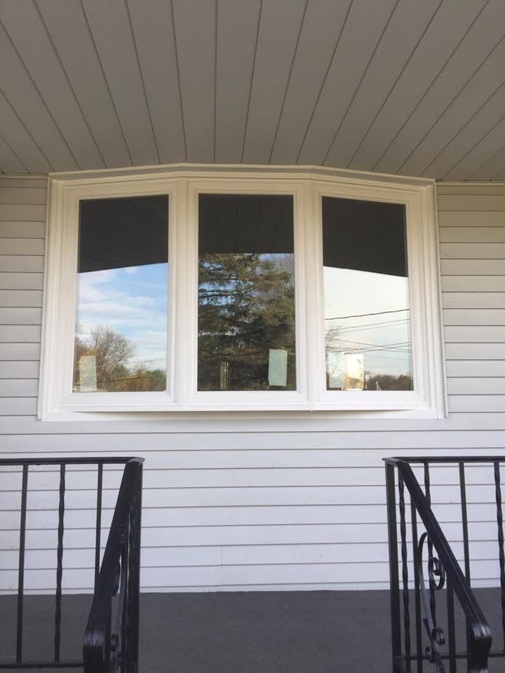 A white bay window on a gray house with black window coverings, viewed from a porch with black railings.