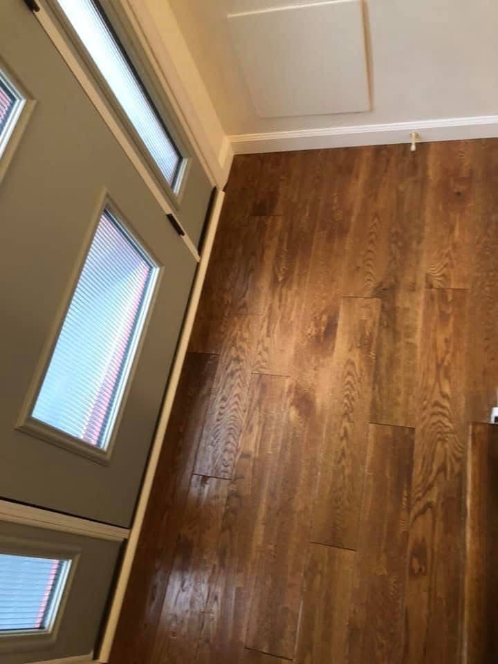 Wooden floor inside a doorway with a light-colored door on the left.  A white trim lines the doorway and ceiling.