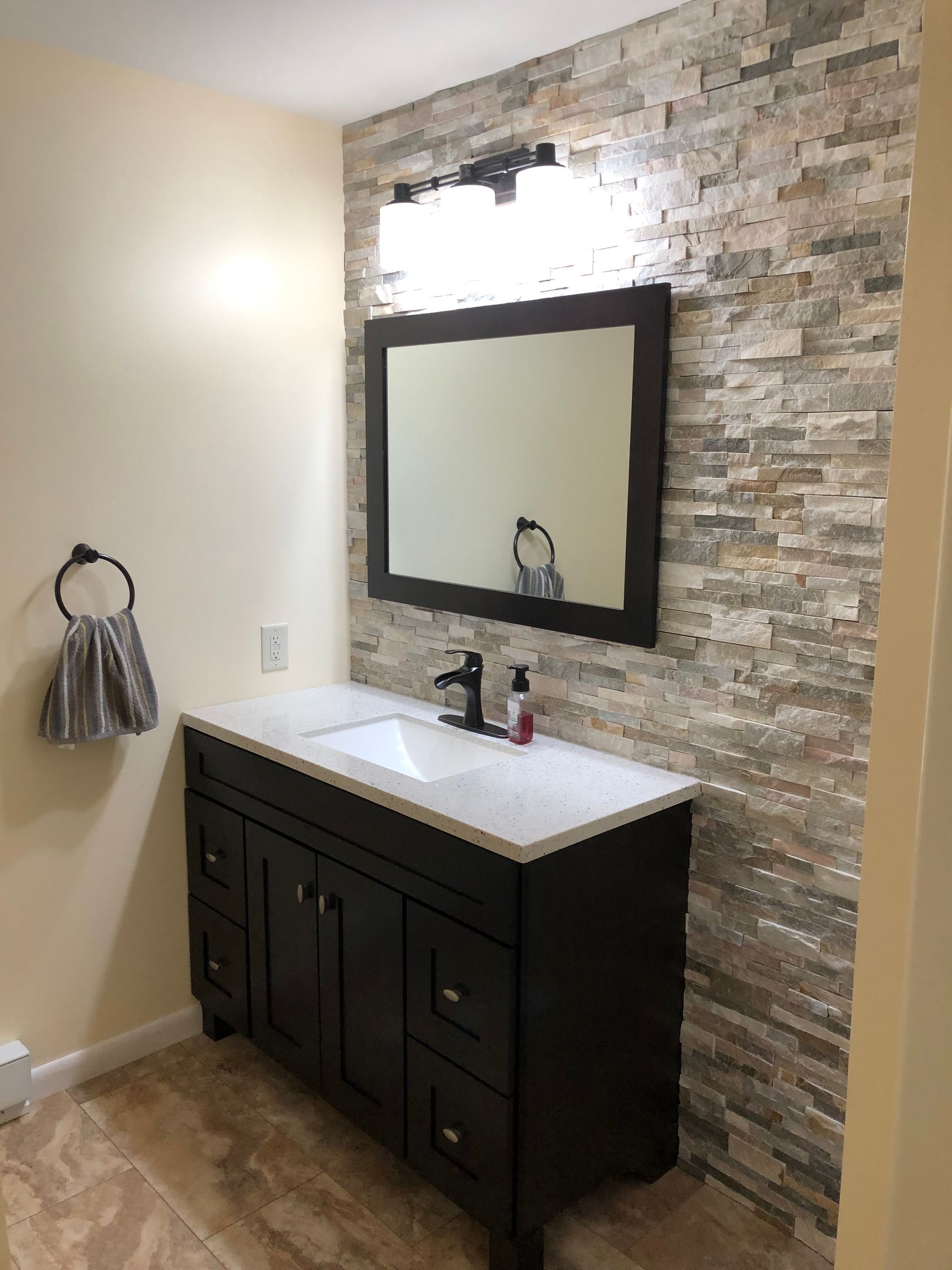 Bathroom with dark brown vanity, white countertop, and stone accent wall behind the mirror and light fixture.