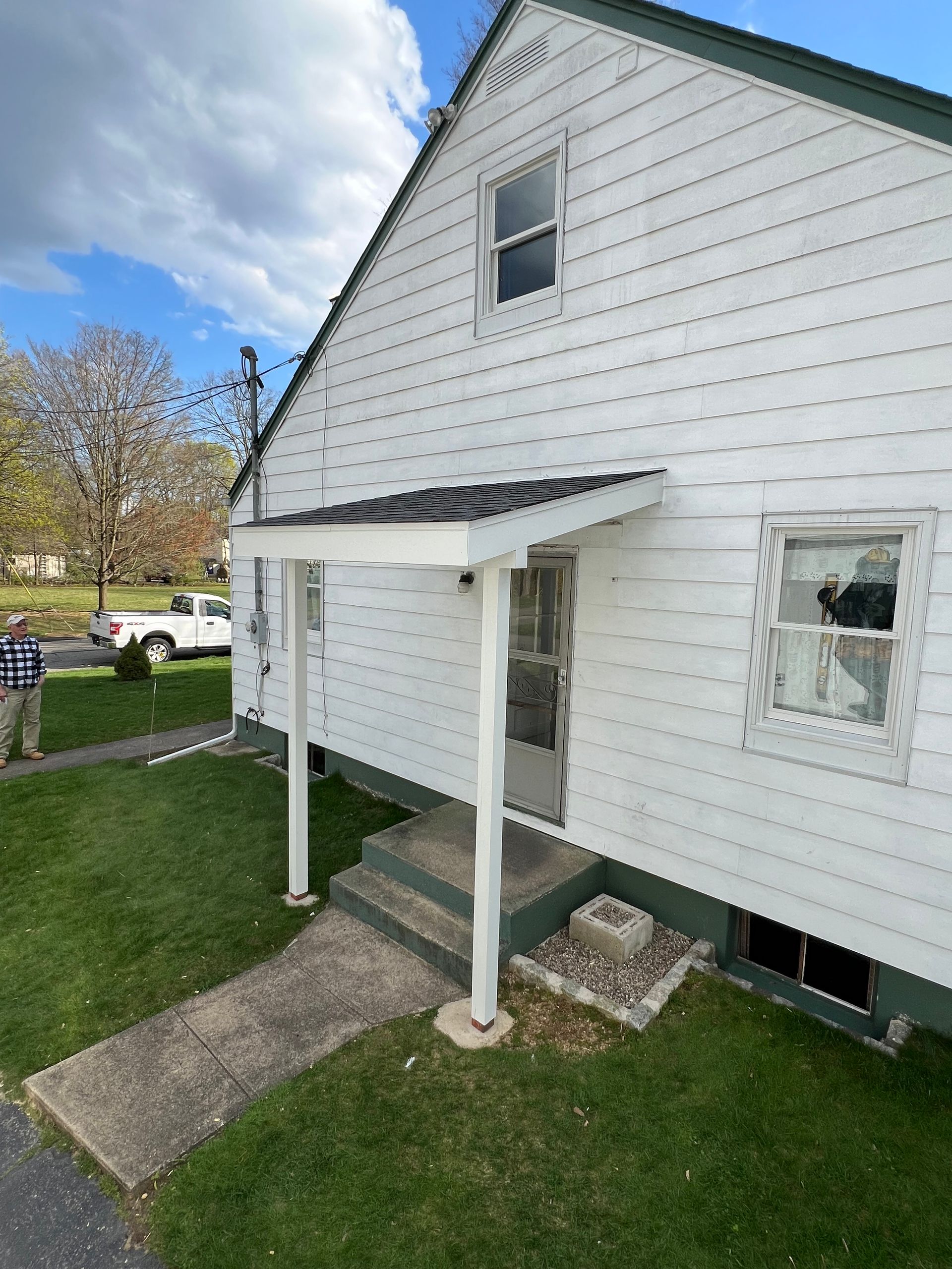 White house with a small porch, steps leading up to a door. Green grass surrounds the house on a cloudy day.