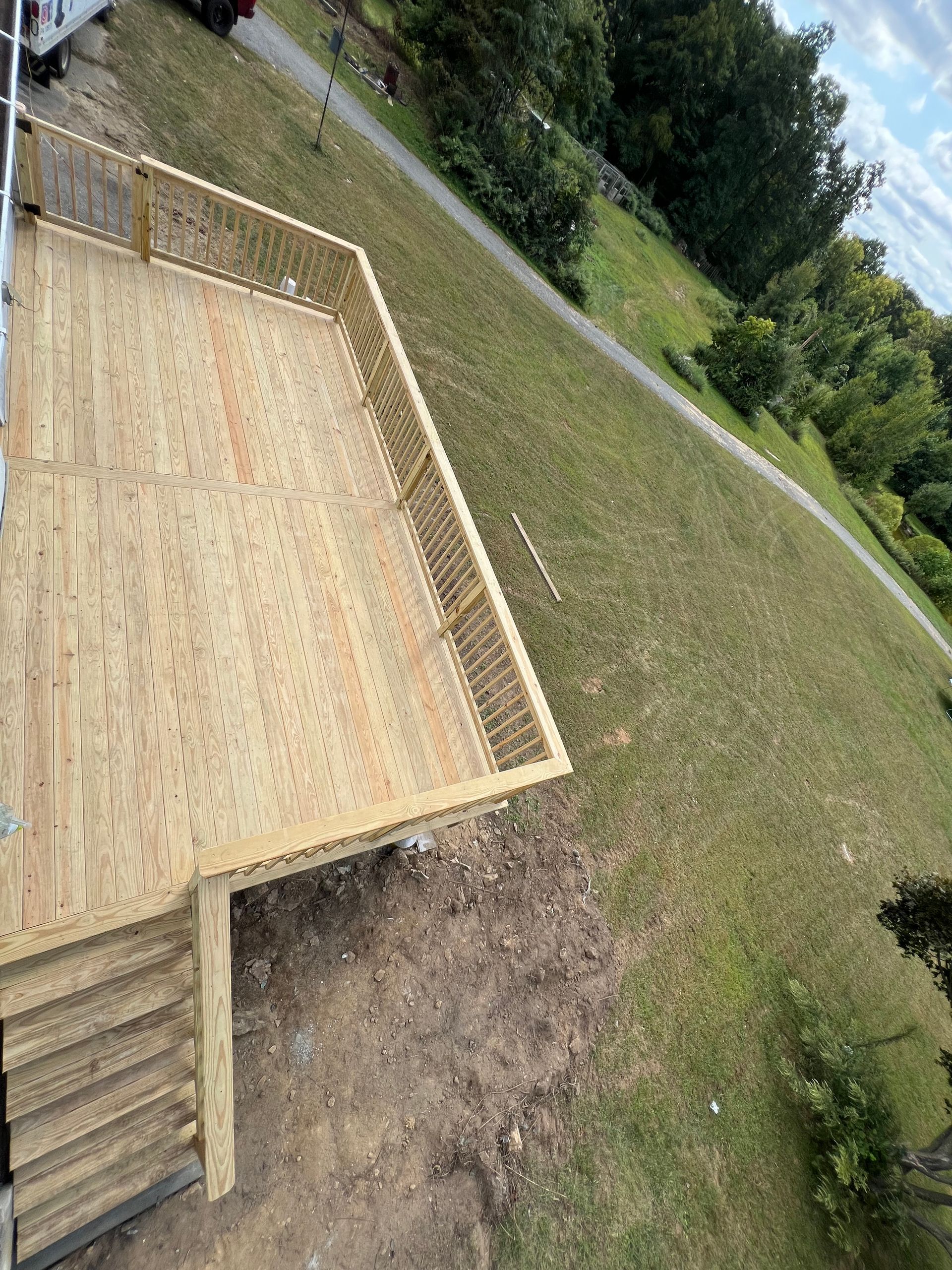Wooden deck with steps leading down to a grassy hill. The deck has a railing and is unpainted.
