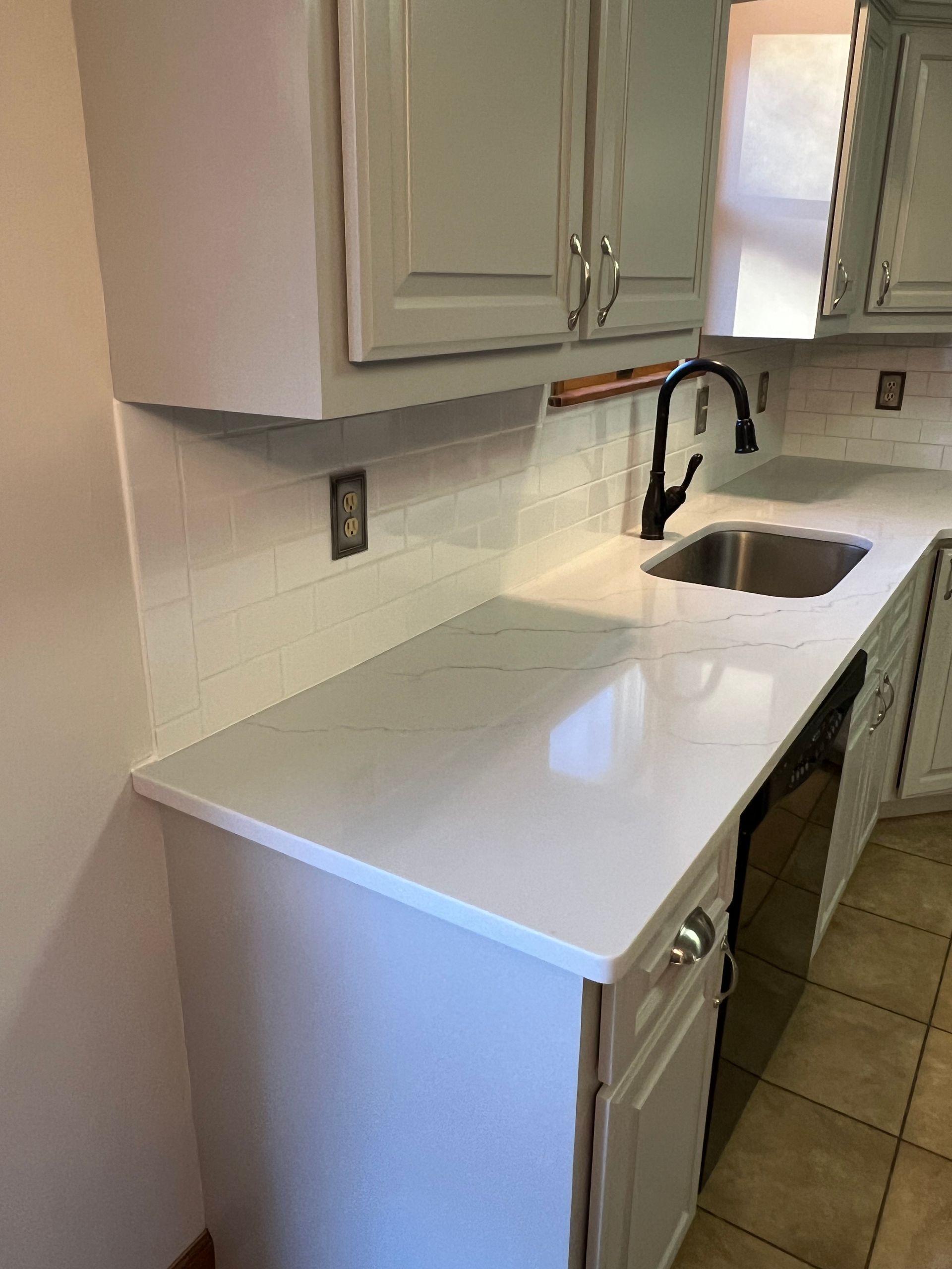 Kitchen renovation featuring white countertops, backsplash, and cabinets painted a light blue-green. A black faucet sits over a stainless steel sink.