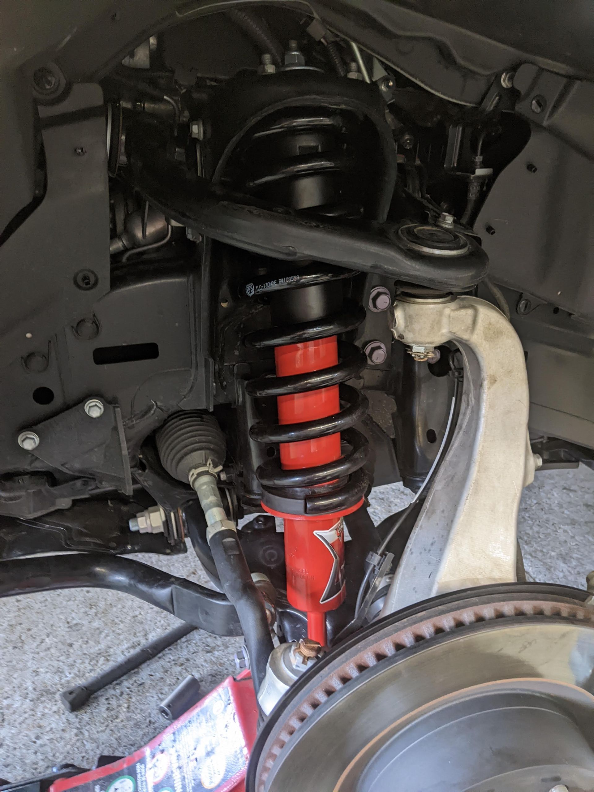 Red suspension coil-over on a truck's front wheel, with black and gray components. — 100% Automotive In South Nowra, NSW